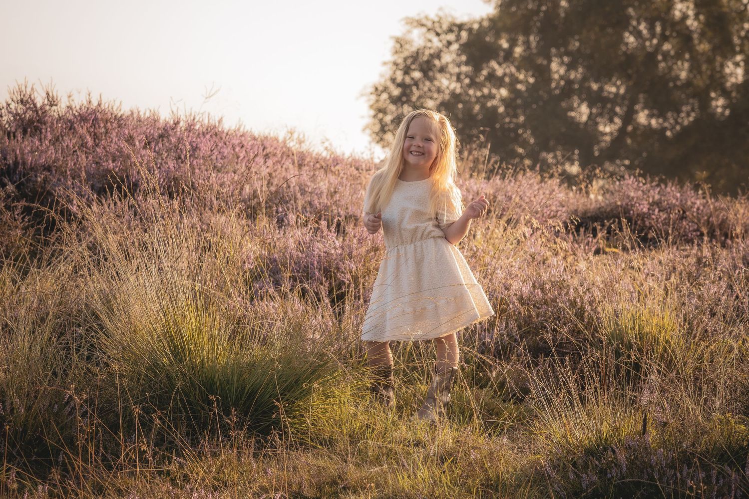 A young child with bright blue eyes sits among fallen autumn leaves.
