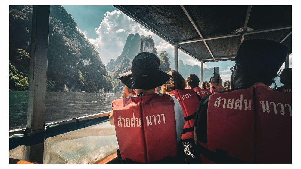 Passengers in red vests ride a tour boat through misty mountains with dramatic peaks in the background.