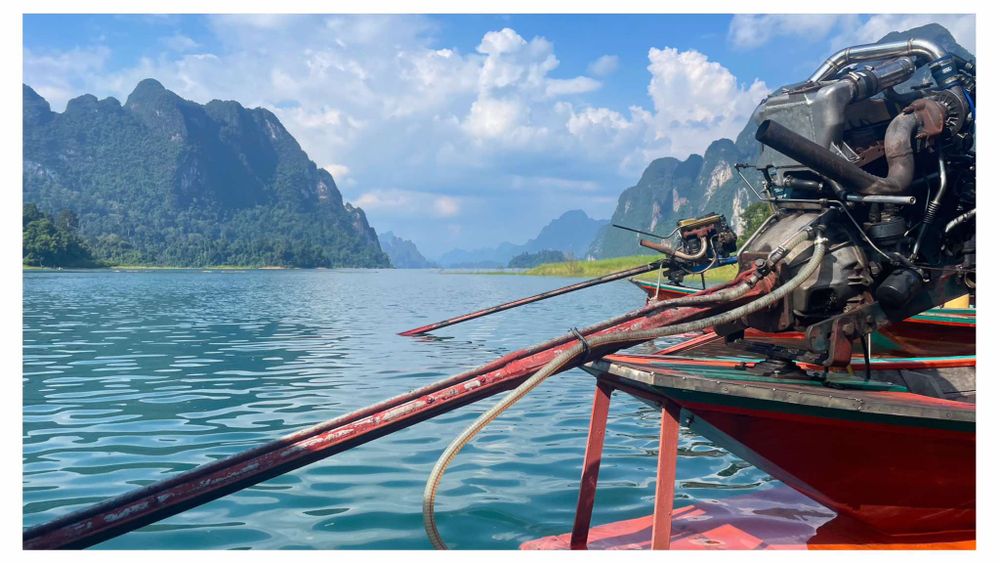 Traditional wooden longtail boat cruising through emerald waters surrounded by dramatic limestone cliffs in Thailand.