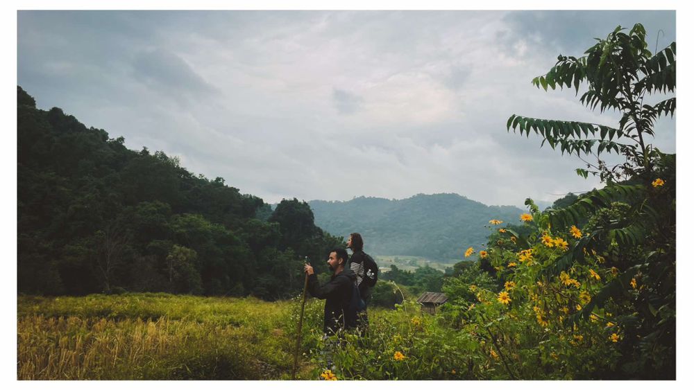 People stand on a hillside overlooking mountains and valleys with wildflowers growing in the foreground.
