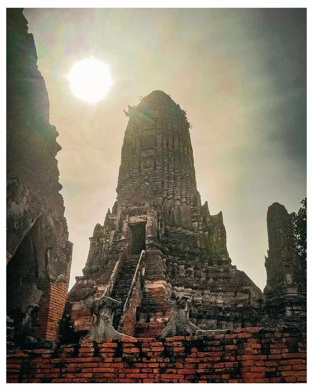 Ancient temple ruins with tall spires silhouetted against a bright sun in a mystical atmosphere.
