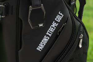Close-up detail of a black golf bag showing embroidered text and zippered compartment.
