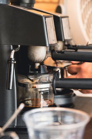 Close-up view of an espresso machine brewing coffee with portafilter and glass containers in soft warm lighting.