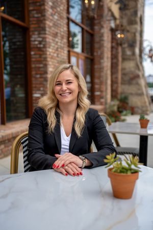 Professional portrait series showing a businesswoman seated at a table with exposed brick and potted plants in background.
