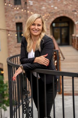 Professional headshots showing a woman in black blazer posing by decorative metal railings with brick architecture.
