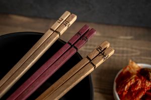 Chopsticks resting on a dark wooden surface with a blurred bowl of red sauce in the background.