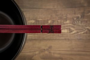 Red chopsticks rest across a black bowl on a rustic wooden table surface.