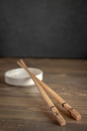 Traditional wooden chopsticks resting on a white ceramic dish against a dark background on wooden surface.