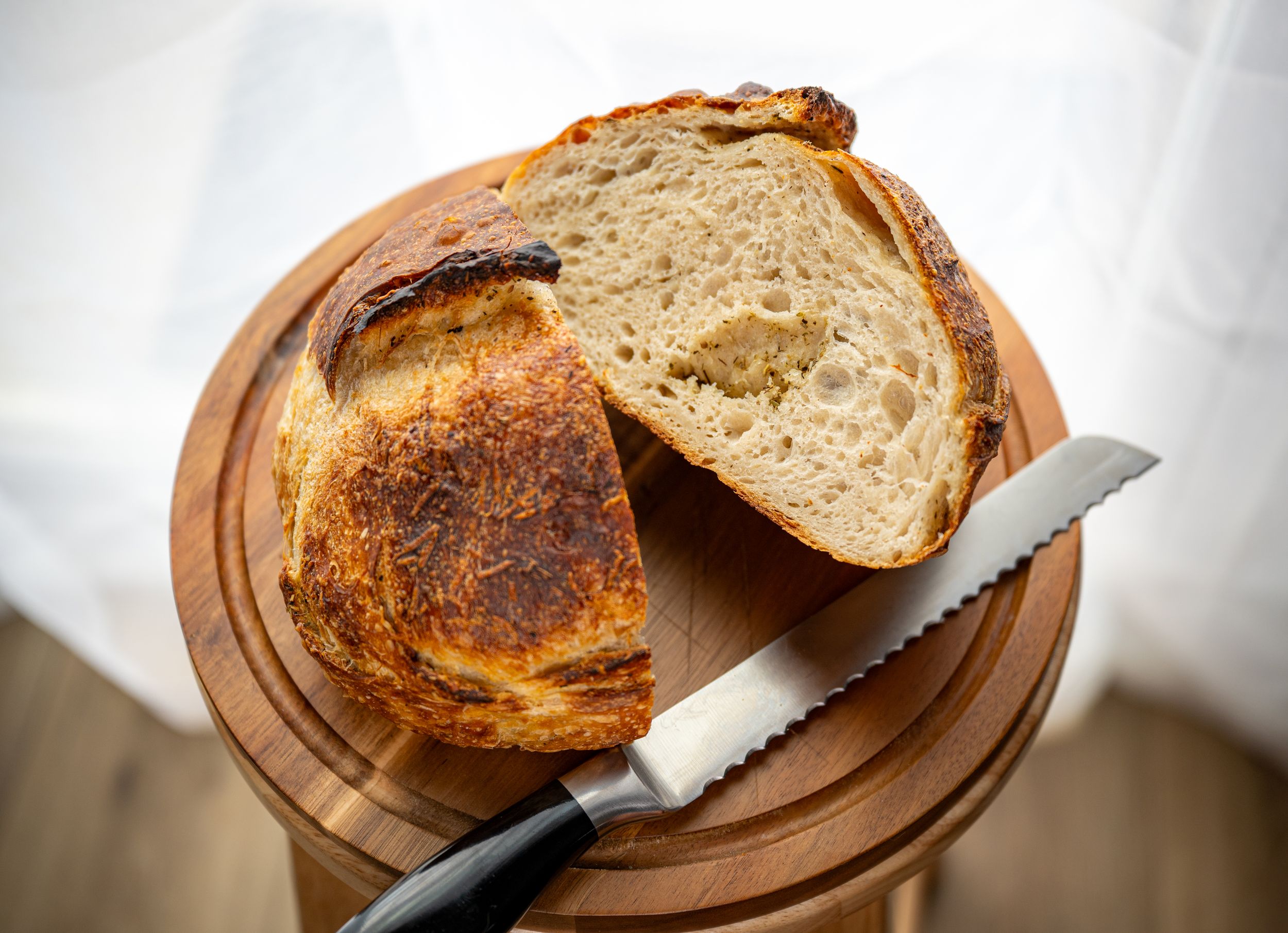 Slicing a freshly baked artisanal sourdough loaf on a round wooden cutting board.
