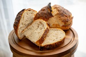 Rustic sourdough bread loaf sliced on wooden cutting board showing crusty exterior and soft interior texture.