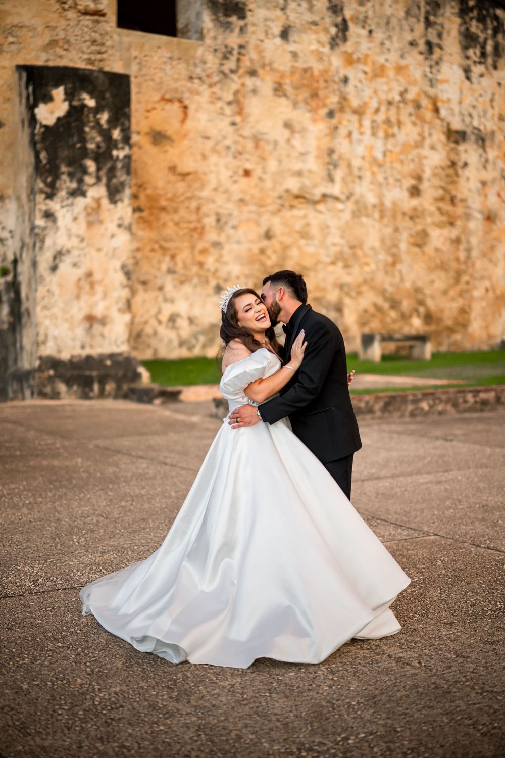 A romantic wedding photo captures an intimate dance between newlyweds near historic stone architecture.
