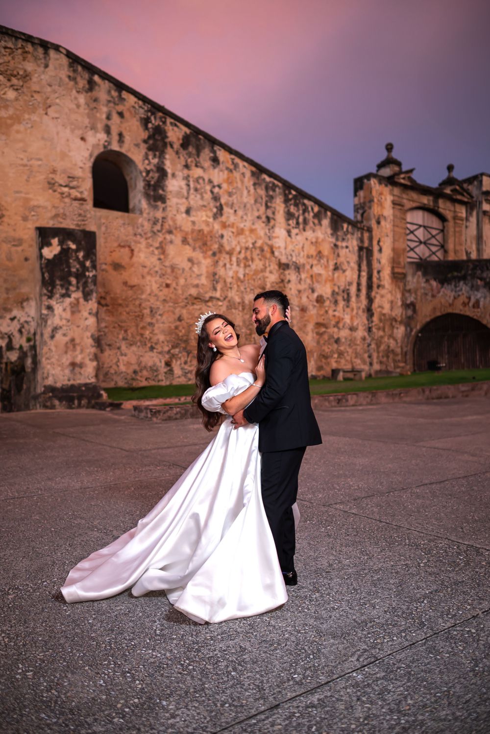 A couple shares an intimate moment during sunset against a historic fortress backdrop.