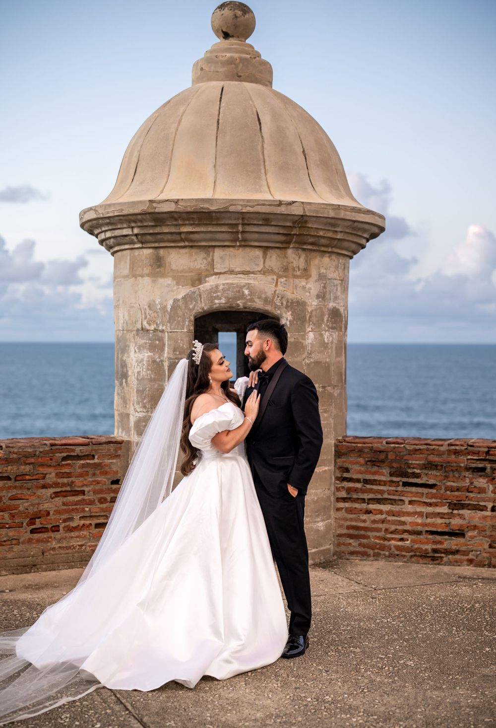A romantic wedding portrait at a historic stone tower overlooking the sea.