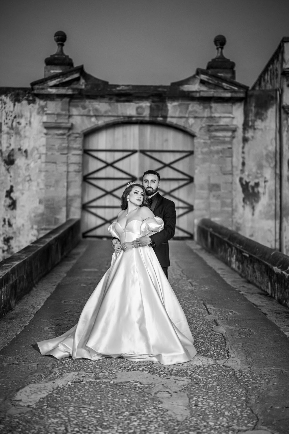 A romantic black and white wedding portrait taken on a historic stone bridge with architectural details.