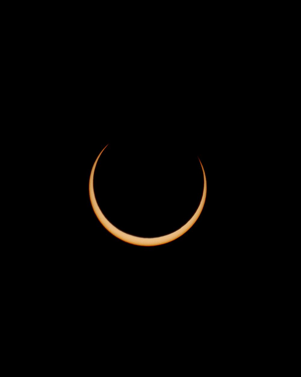 Crescent solar eclipse glowing orange against black sky background.