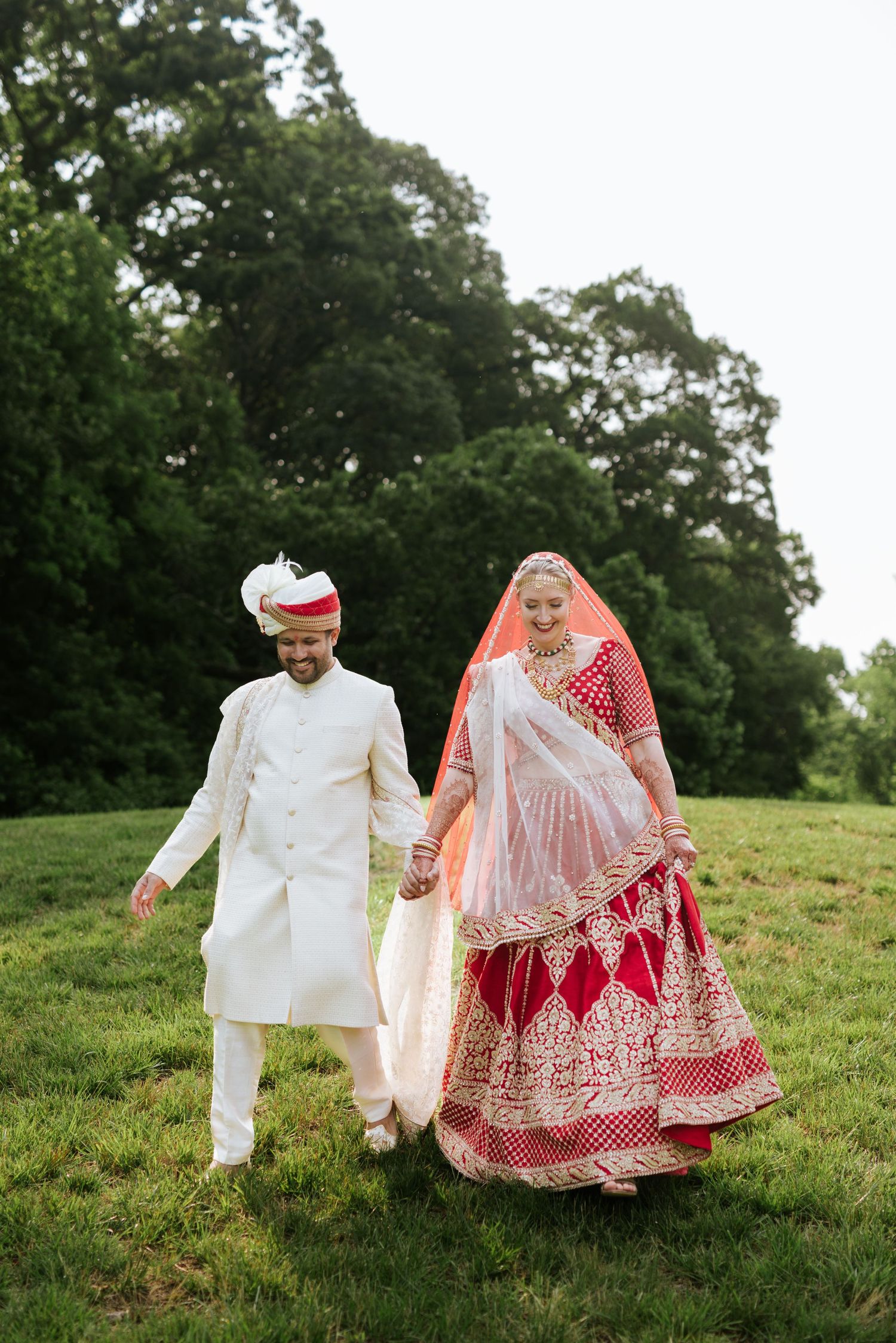 A joyful couple in traditional attire strolls through lush greens at The Drexelbrook Catering & Event Center—timeless elegance in Philly.