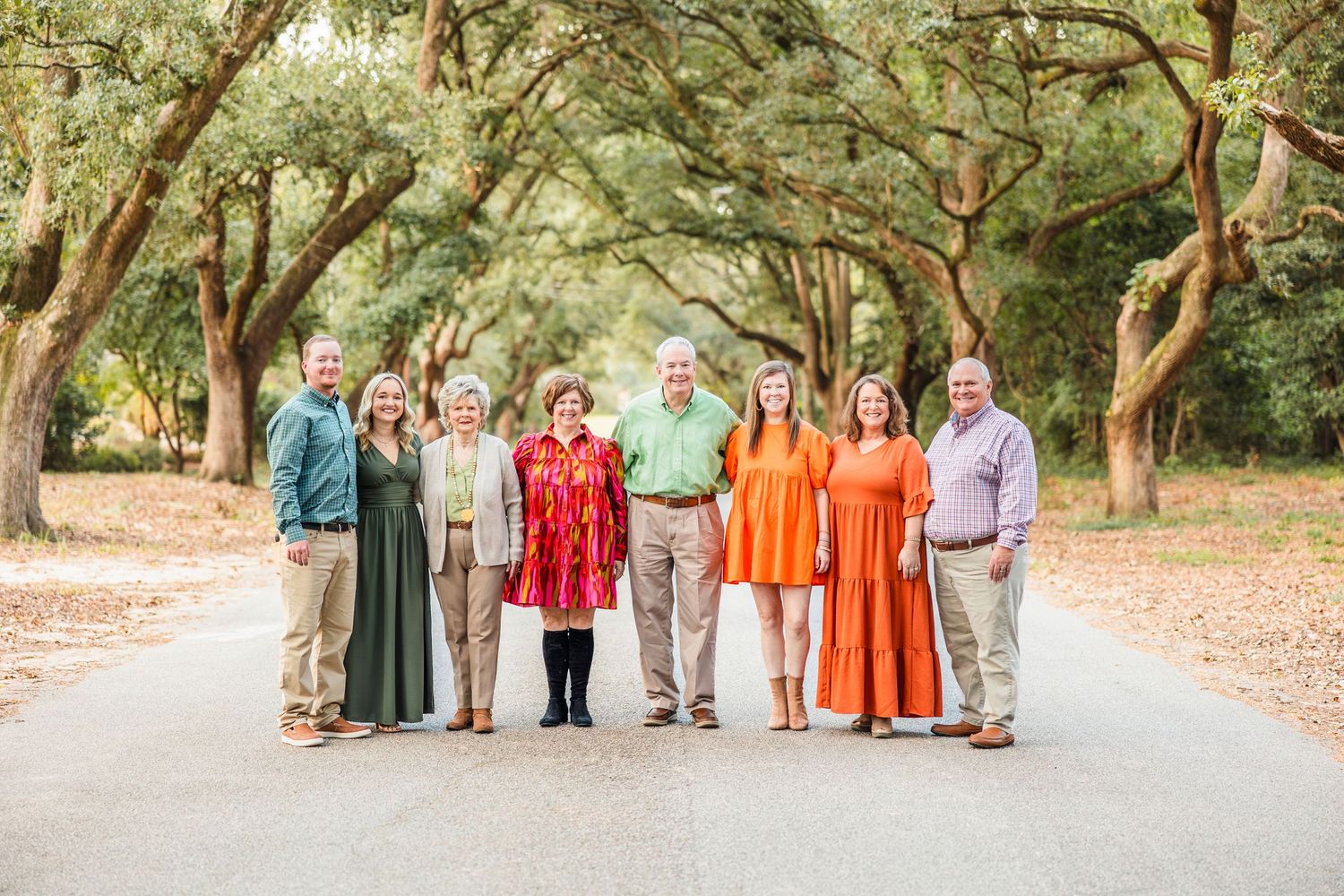 Large family group photo with coordinated outfits standing among oak trees.