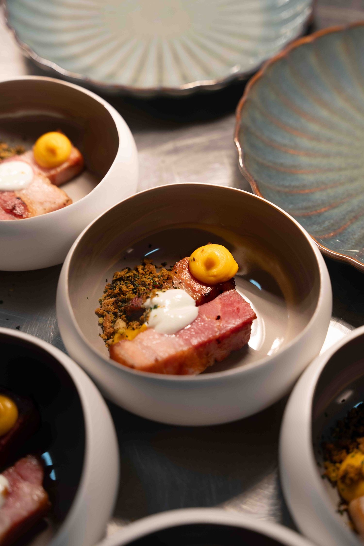 Gourmet meat dish with yellow garnish plated in stylish ceramic bowls.