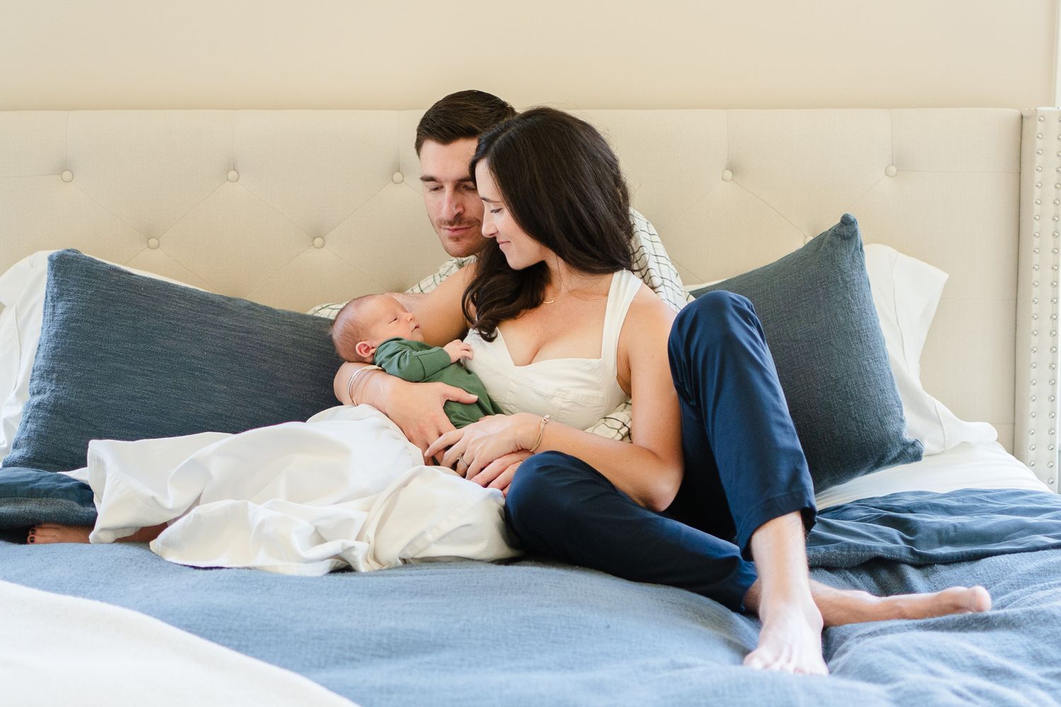 Parents curl up on their bed in an at-home newborn session.