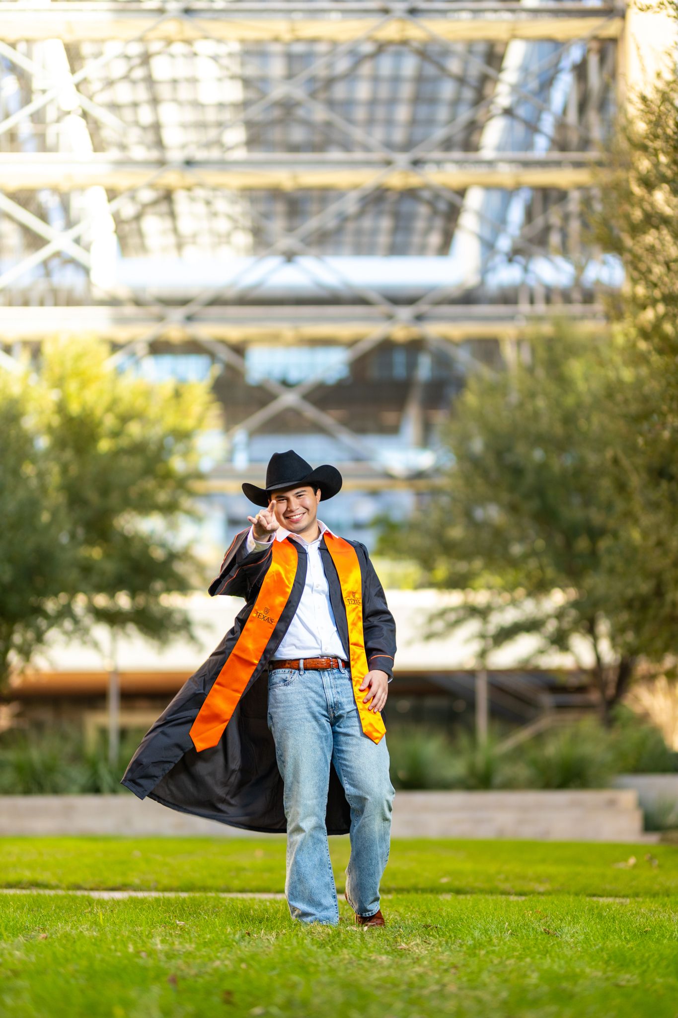 Person wearing cowboy hat and orange vest strikes casual pose on green grass lawn.