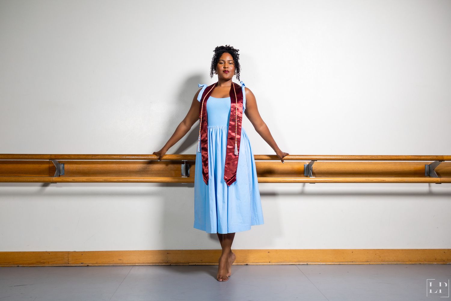 Person in light blue dress poses against white wall with wooden railing.