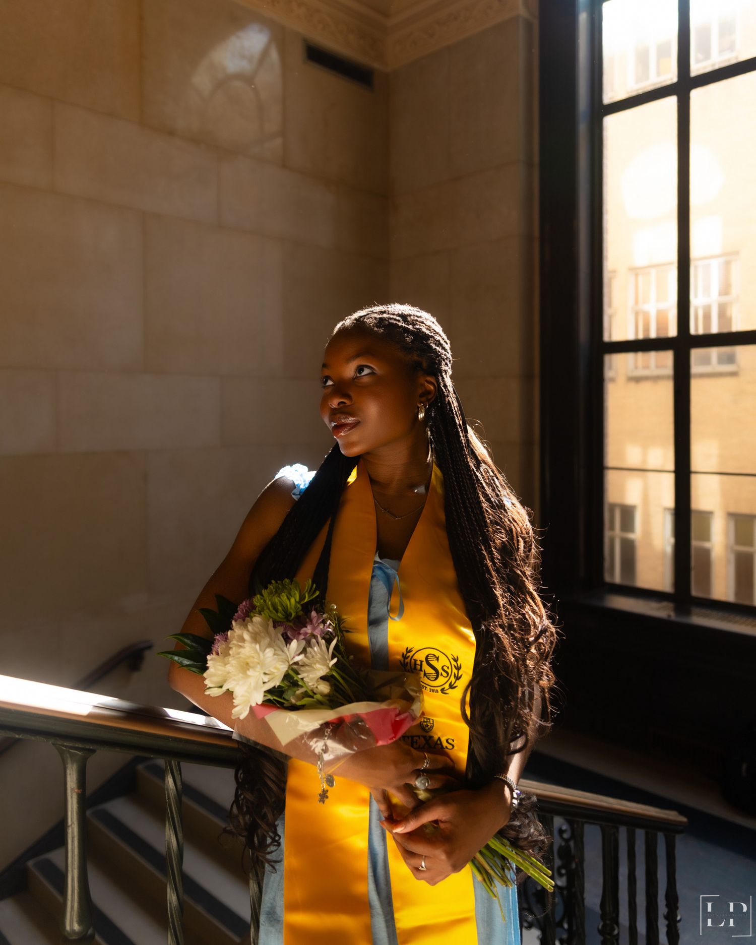 Sunlit graduation photos featuring yellow academic regalia and flowers in a stairwell.