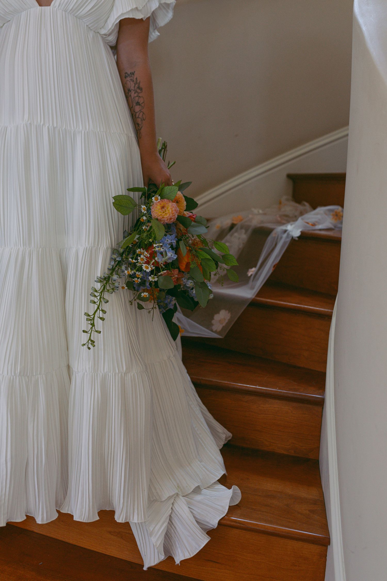 Detail shot of white wedding dress and orange floral bouquet on wooden staircase.