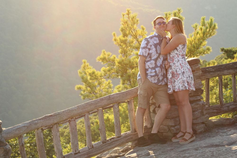 A couple enjoys a sunset moment together on a scenic overlook with golden light.