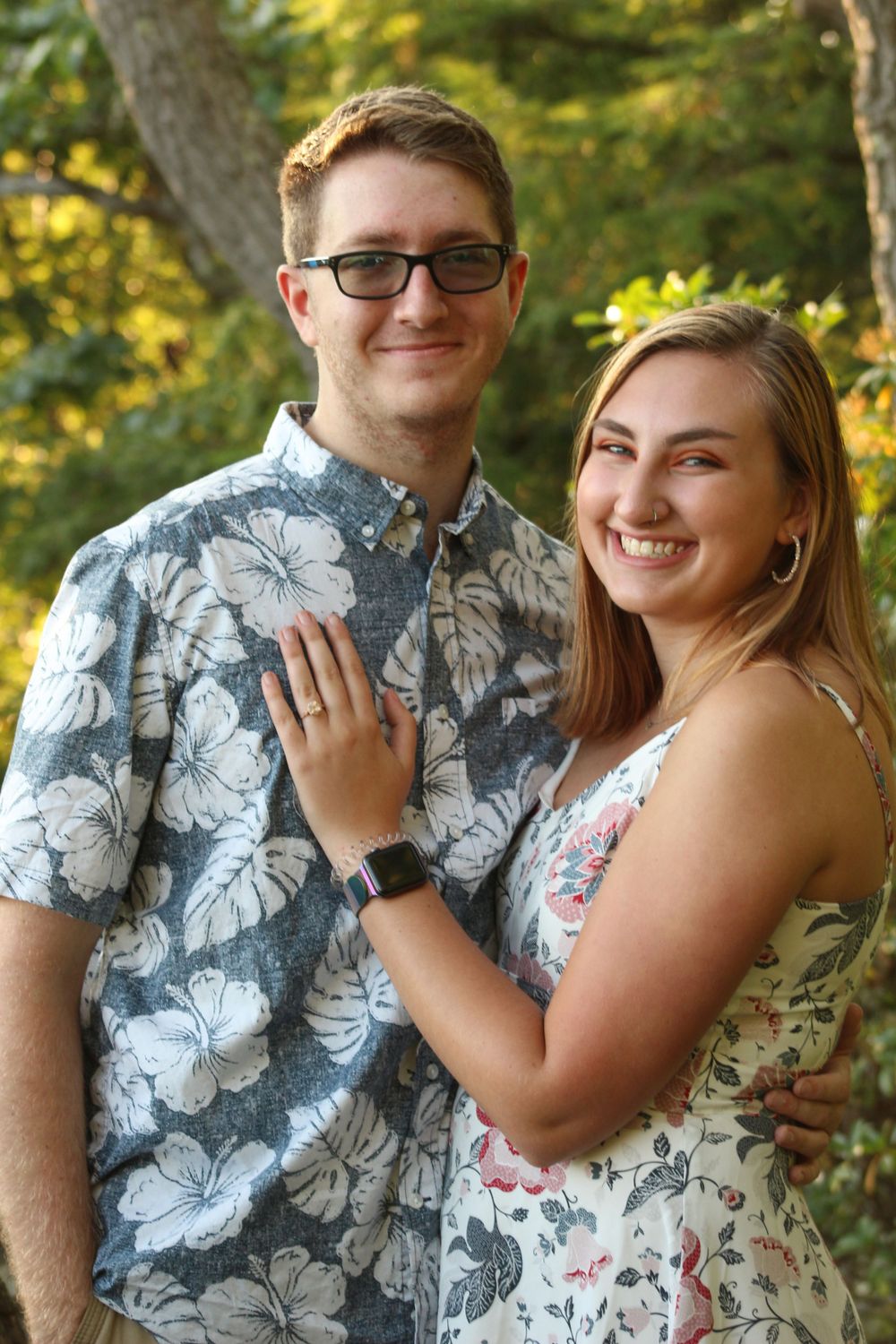 A happy couple in coordinating floral patterns poses for an engagement photo outdoors.