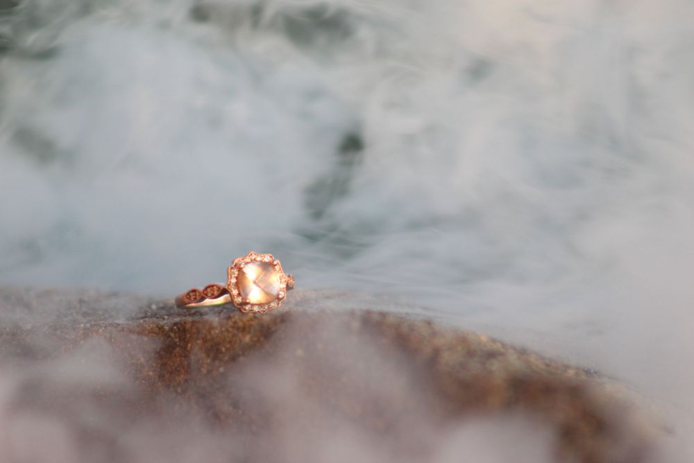 Sparkling diamond engagement ring sitting on a misty surface in soft lighting.
