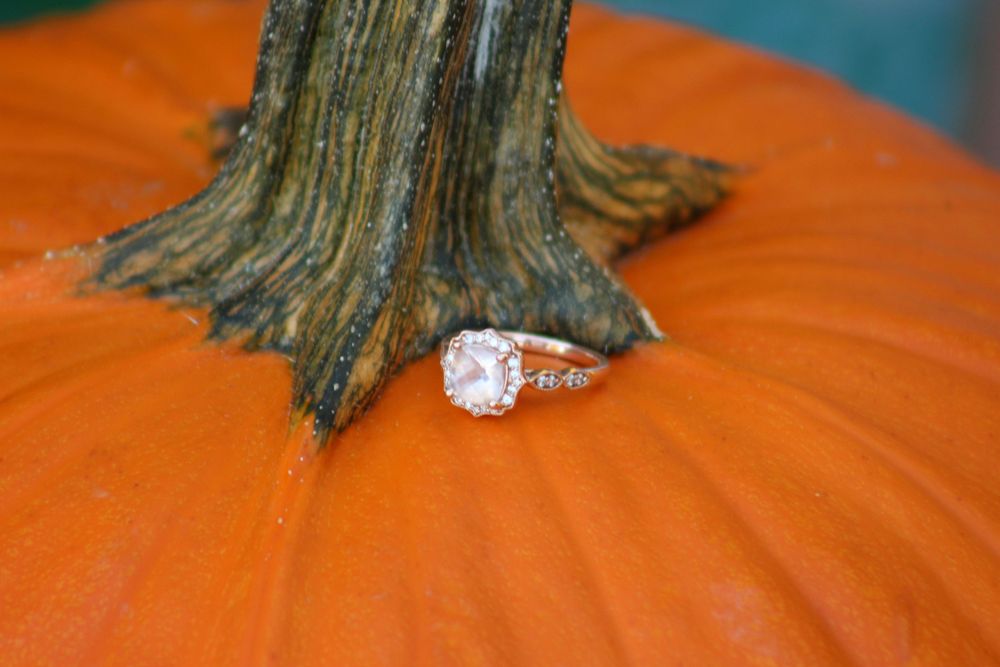 Diamond engagement ring resting against the stem of a bright orange pumpkin.