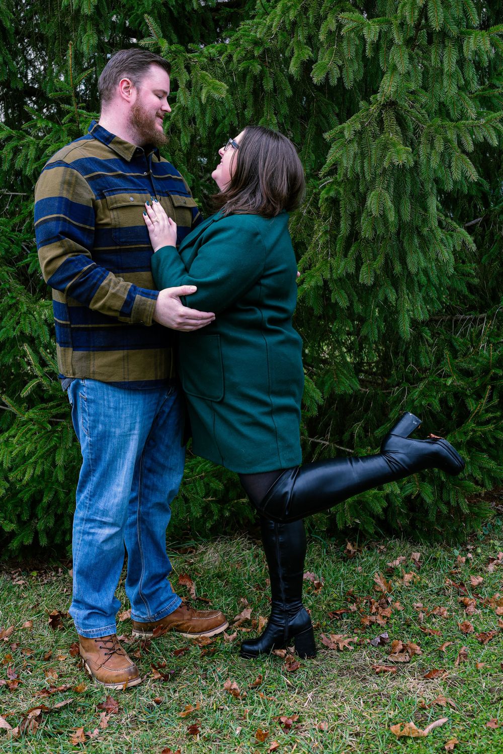 Couple embracing outdoors against a backdrop of evergreen trees.