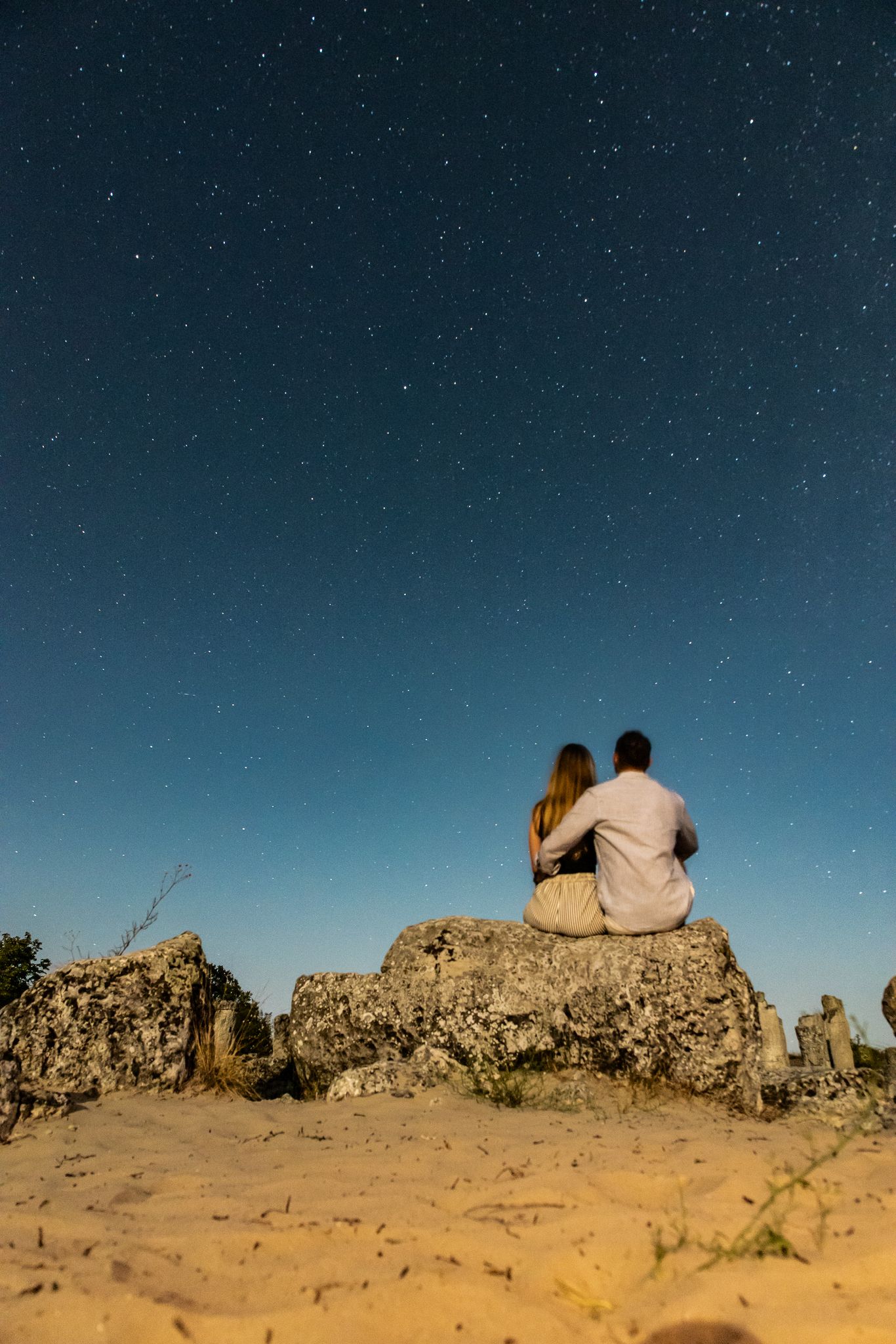 Couple stargazing on a rock among sandy dunes
