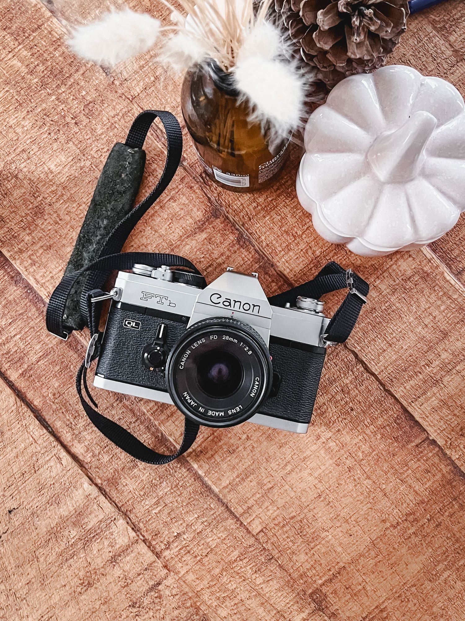 A vintage silver film camera with black leather strap sits on a rustic wooden surface next to white decorative items.