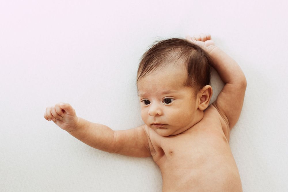 Newborn baby stretching arms while lying on white background.