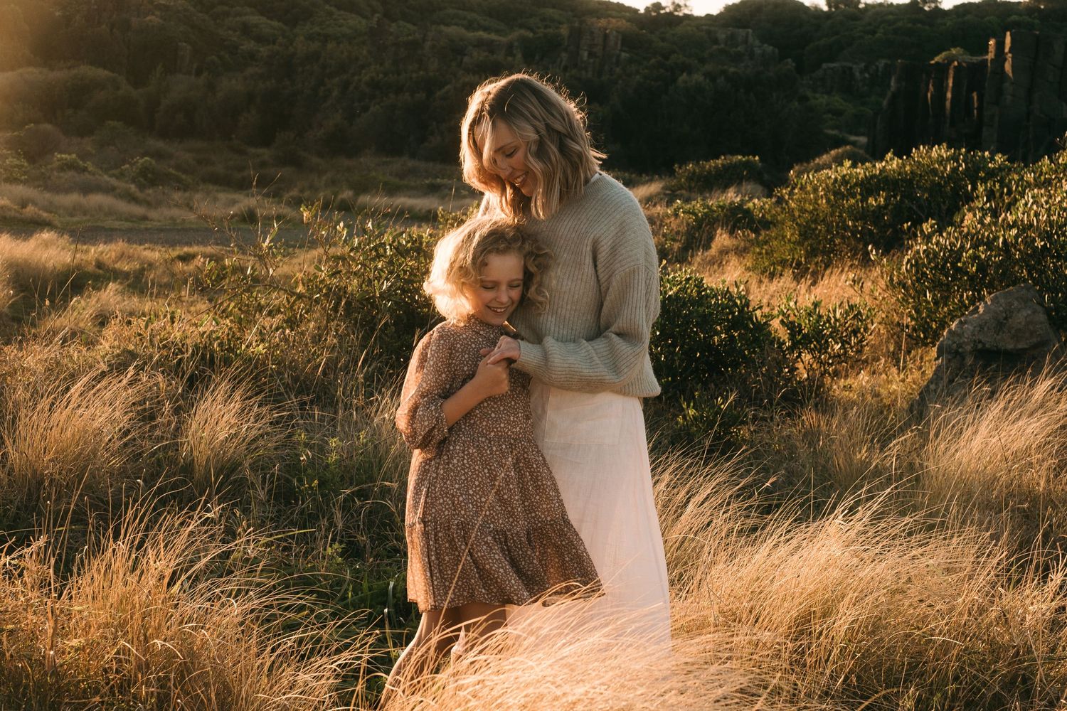 A tender embrace captured in golden light amidst tall grass during sunset.