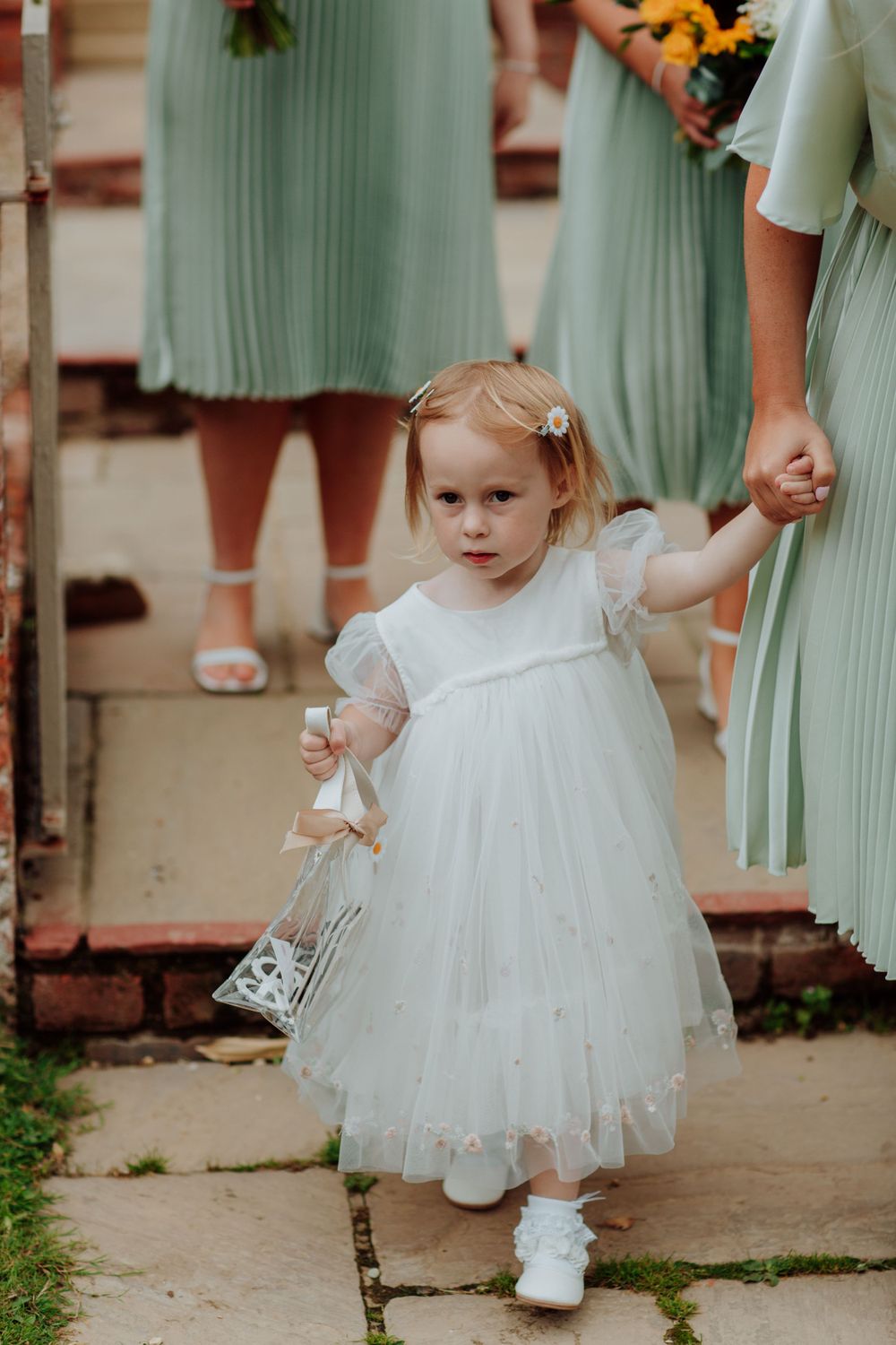 Small flower girl in white dress holds hands with attendants in mint green dresses.
