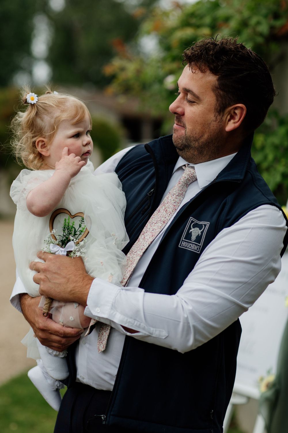 Tender moment between toddler in white dress and adult during wedding celebration. Houchins wedding venue