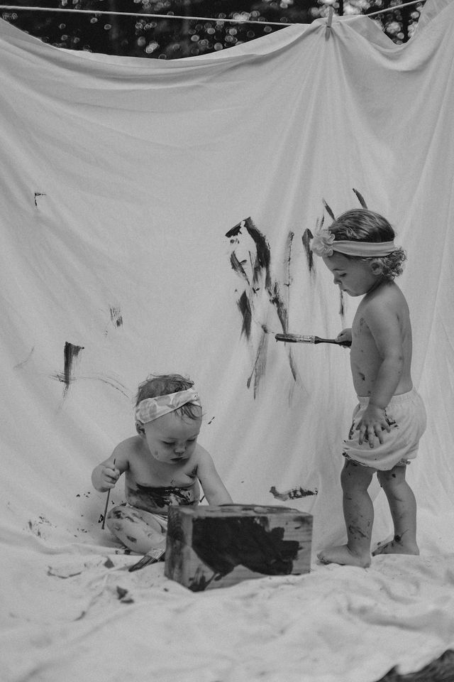Two small children play together against a white backdrop in a vintage black and white photograph.