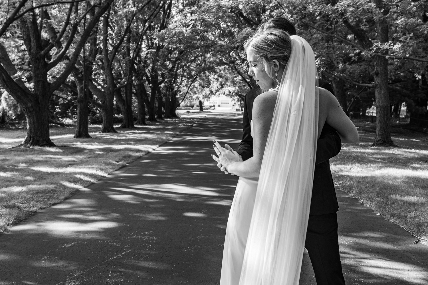 Wedding couple walks along a tree-lined path in a romantic outdoor setting.