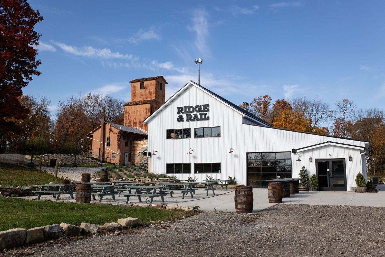 A panoramic view of a white barn and farm buildings with picnic tables and trees in autumn scenery.