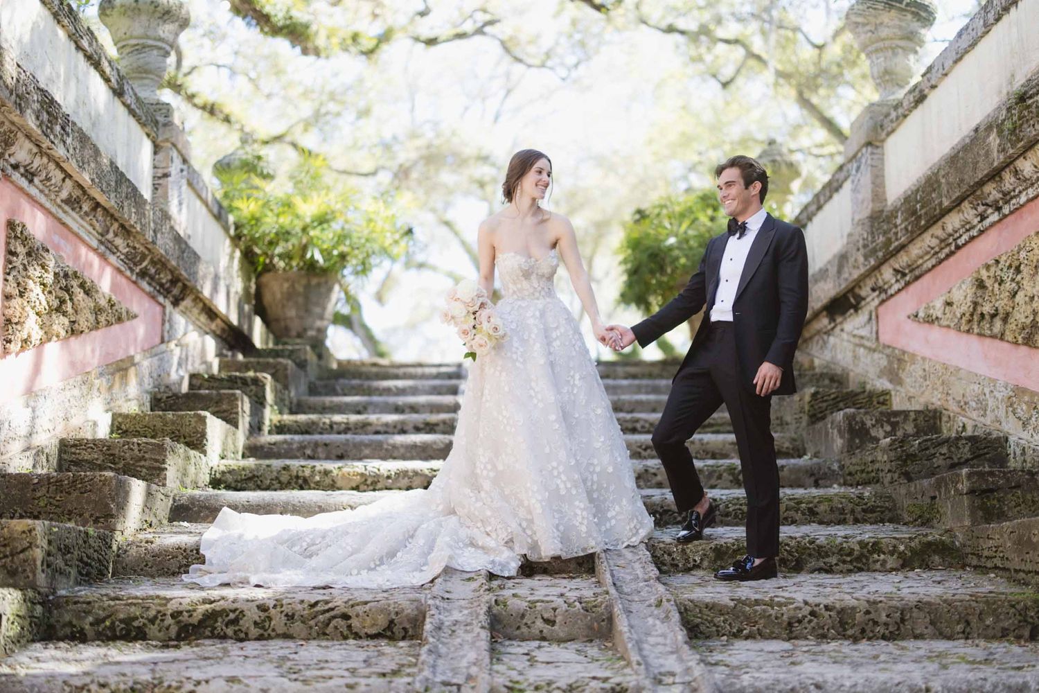 Romantic wedding couple pose on stone staircase surrounded by blooming trees.