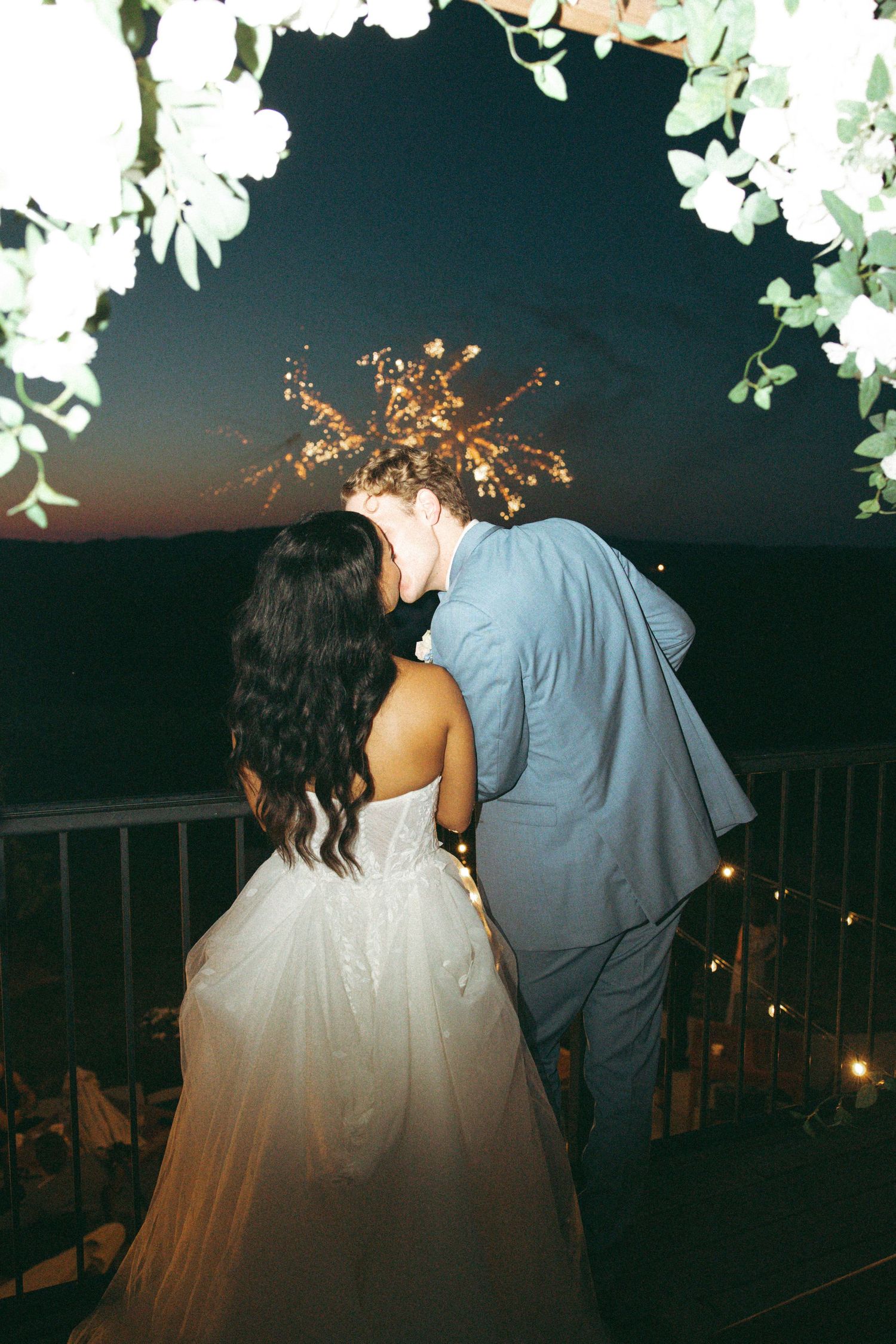Couple shares romantic moment under glowing lights and floral decorations at outdoor wedding venue.