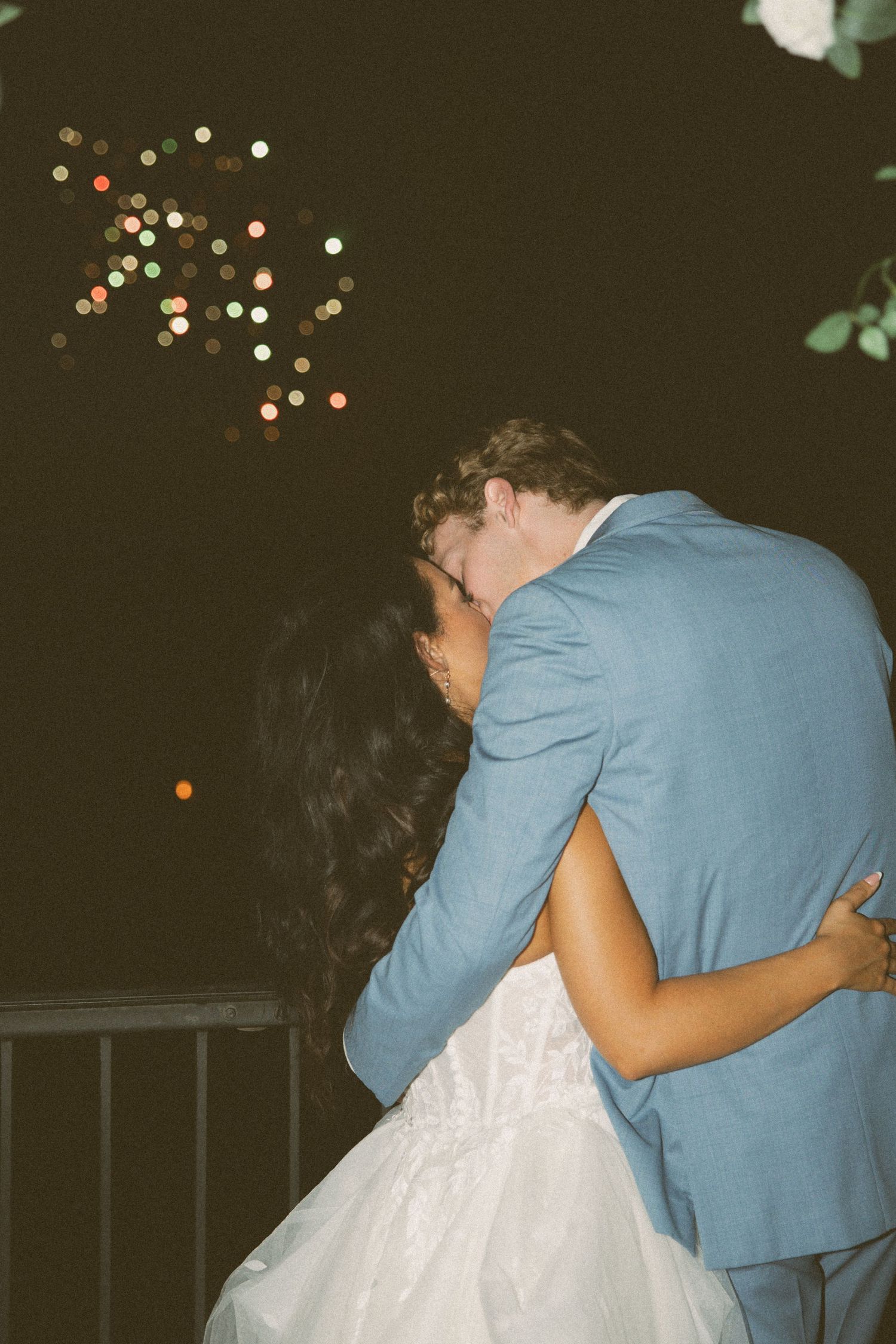 Couple embraces under twinkling lights on outdoor terrace during evening celebration.