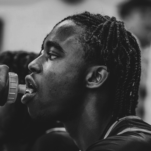 Black and white close-up of a young man drinking from a water bottle.