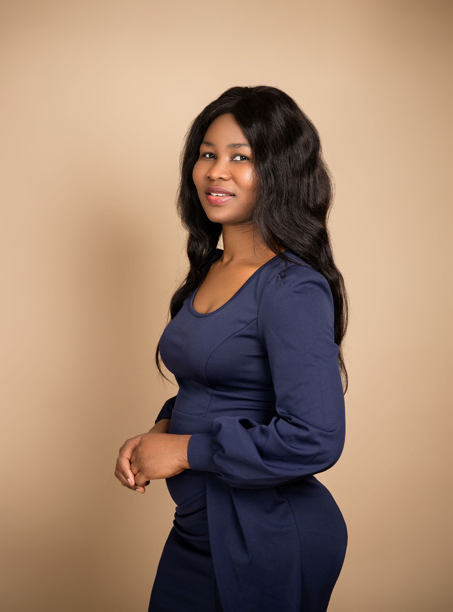 Studio portrait of a person in a navy blue outfit against a beige background.