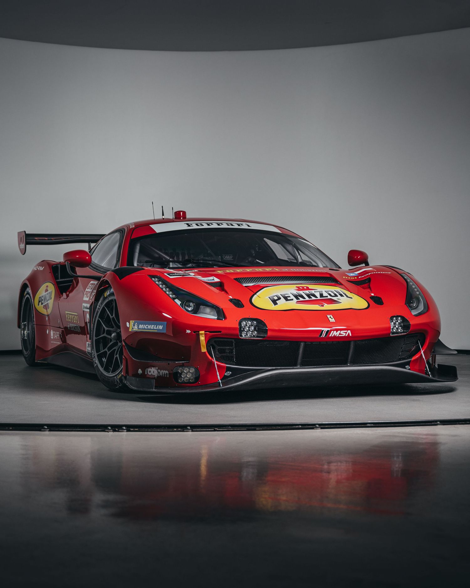Red Ferrari racing car showcased in dramatic studio lighting against grey background.