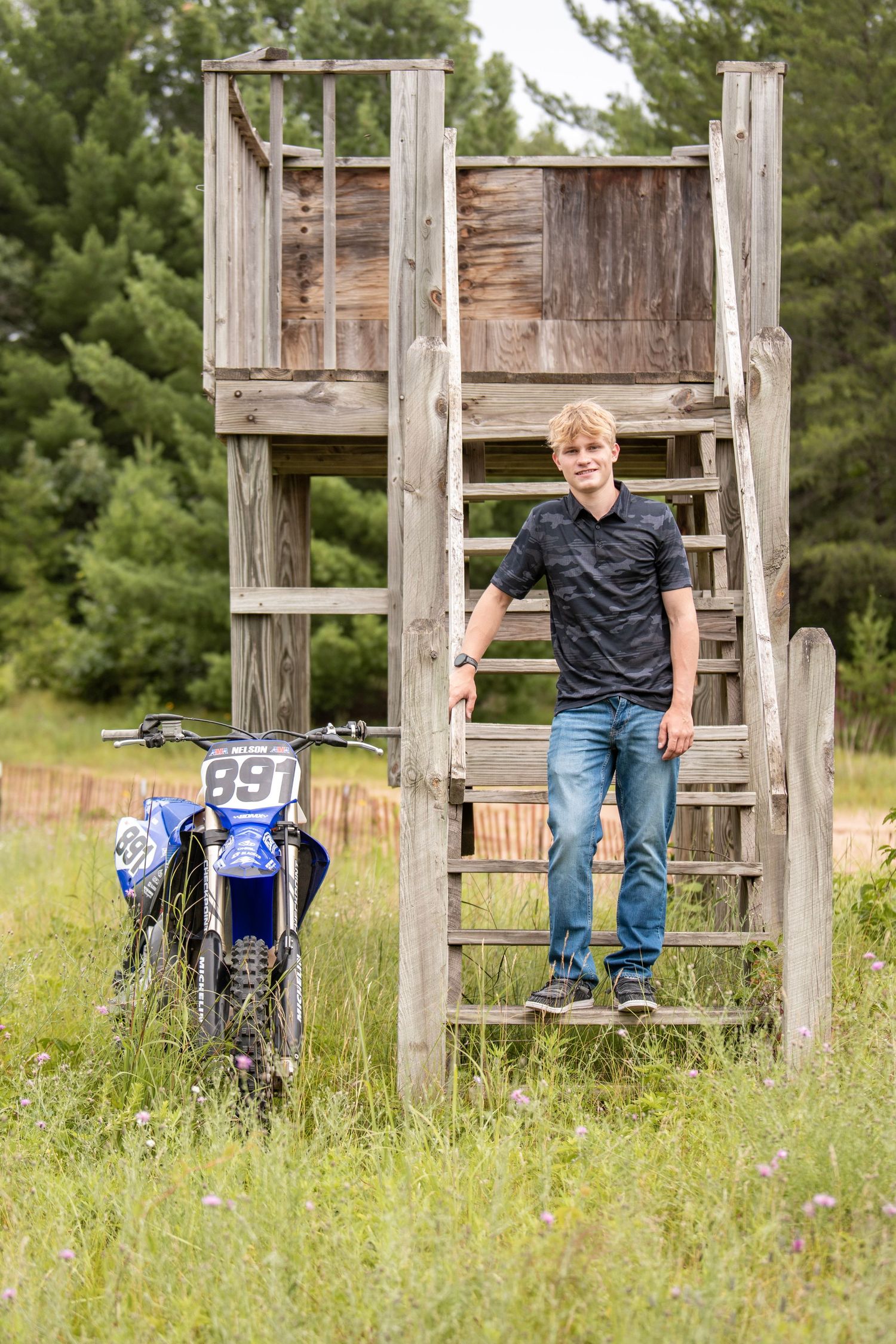 Rural scene with wooden structure and dirt bike in tall grass field.