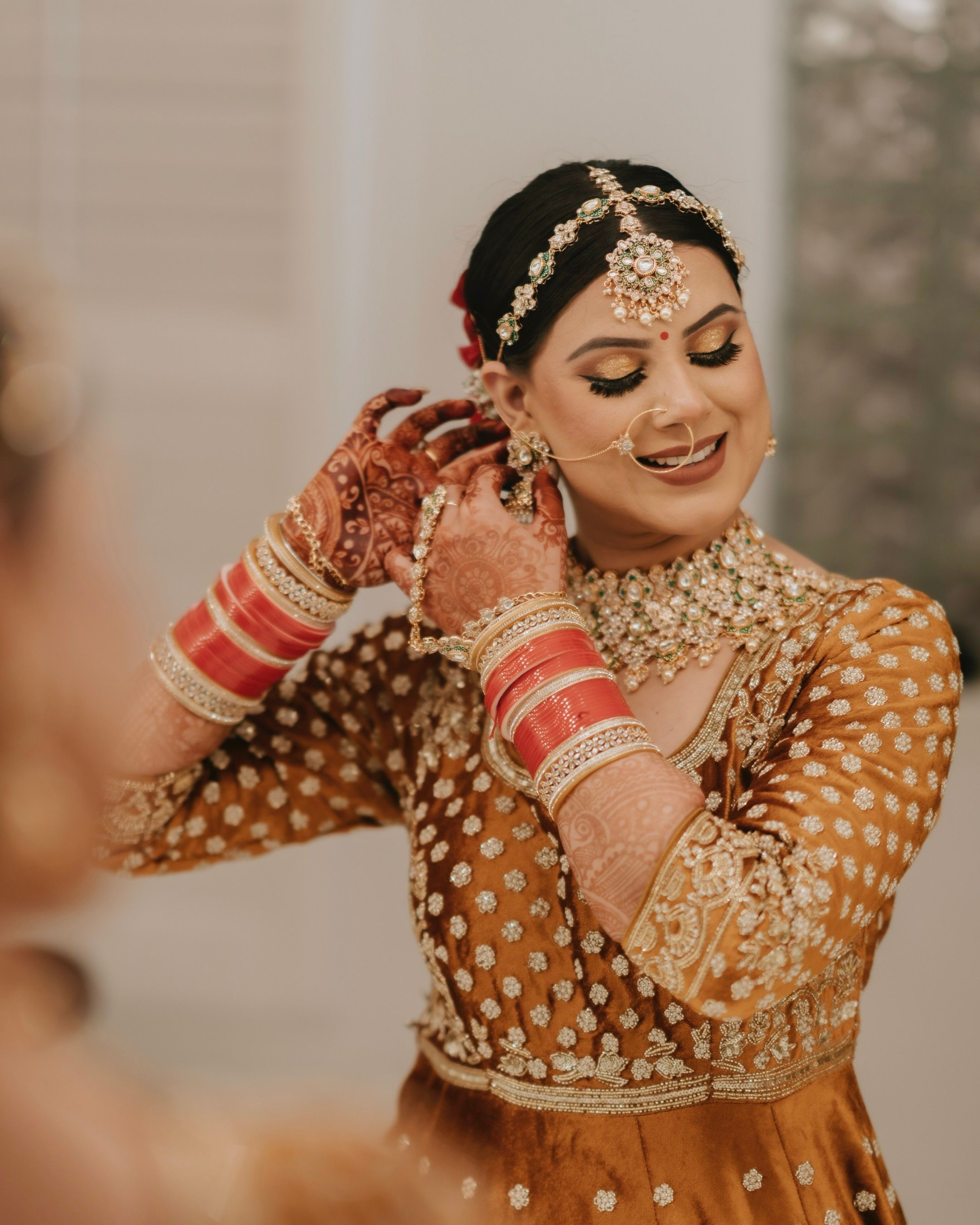 Traditional Indian bride wearing ornate gold jewelry and henna adjusts her earrings.