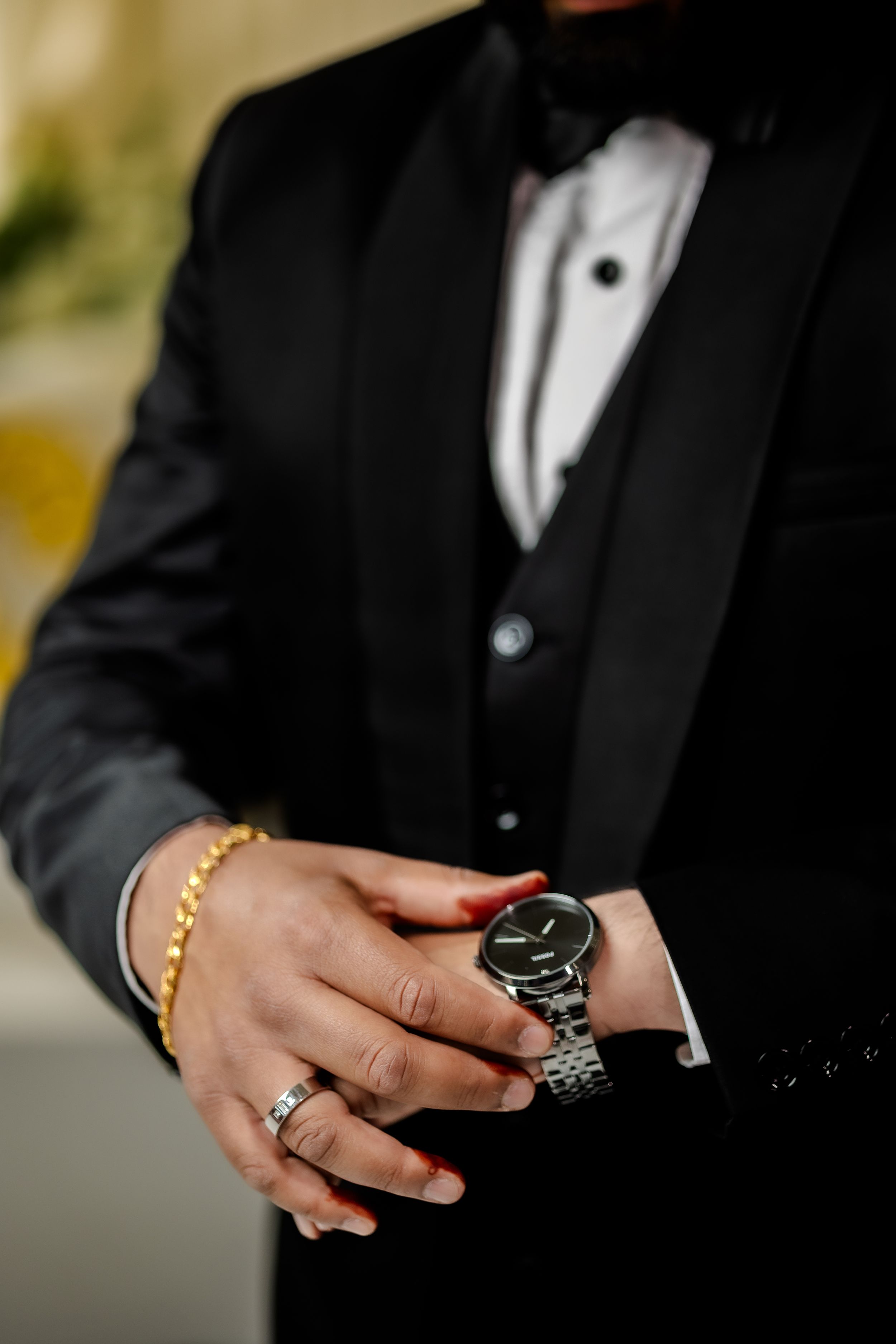 Close-up of hands wearing jewelry and watch with black tuxedo sleeve.